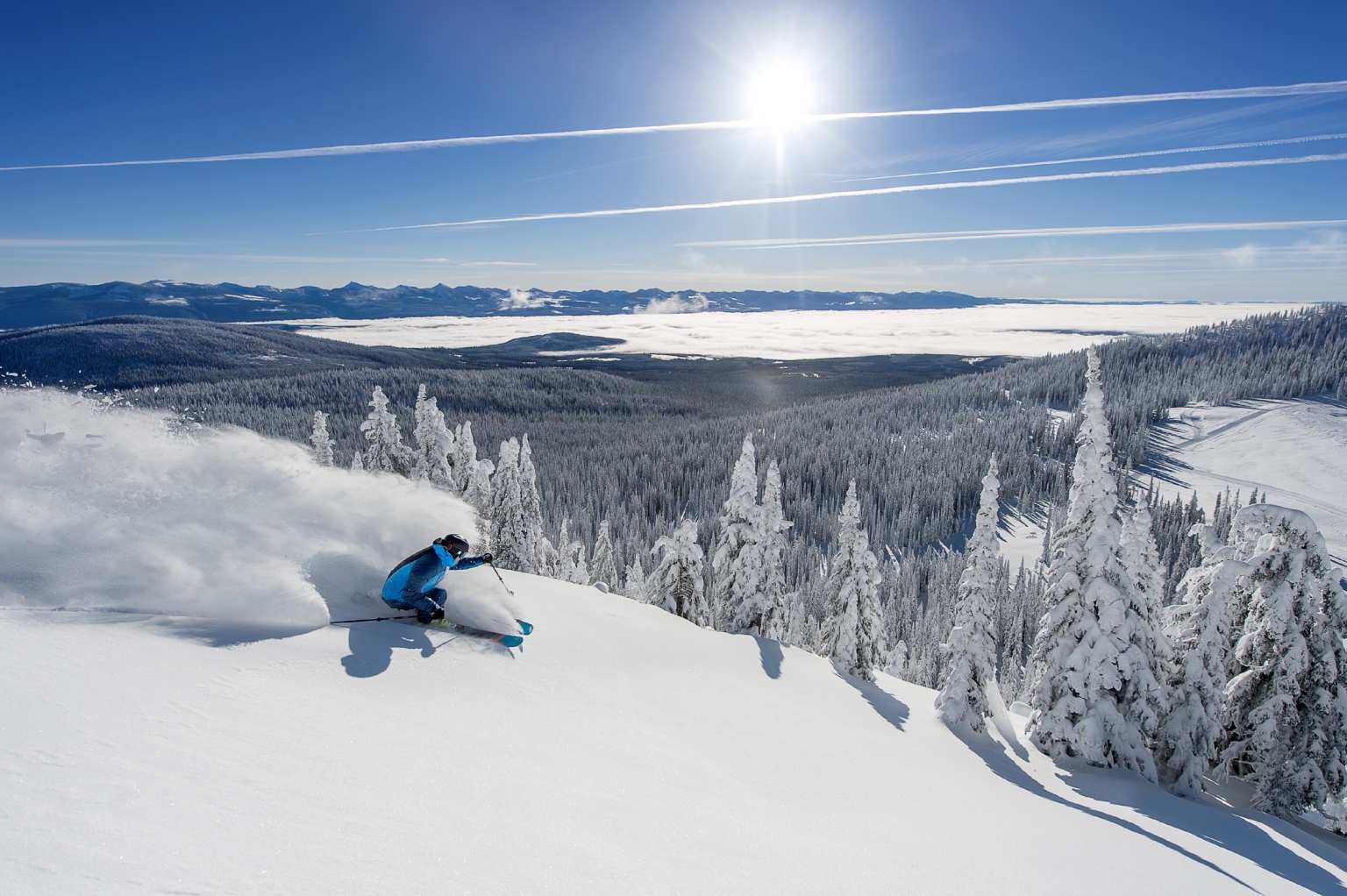 A skier takes large, sweeping powder turns on a bluebird day at Big White Ski Resort.