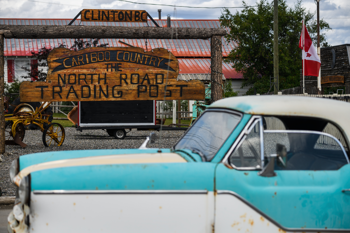 A old blue pick up truck in front of a wooden sign that reads, 