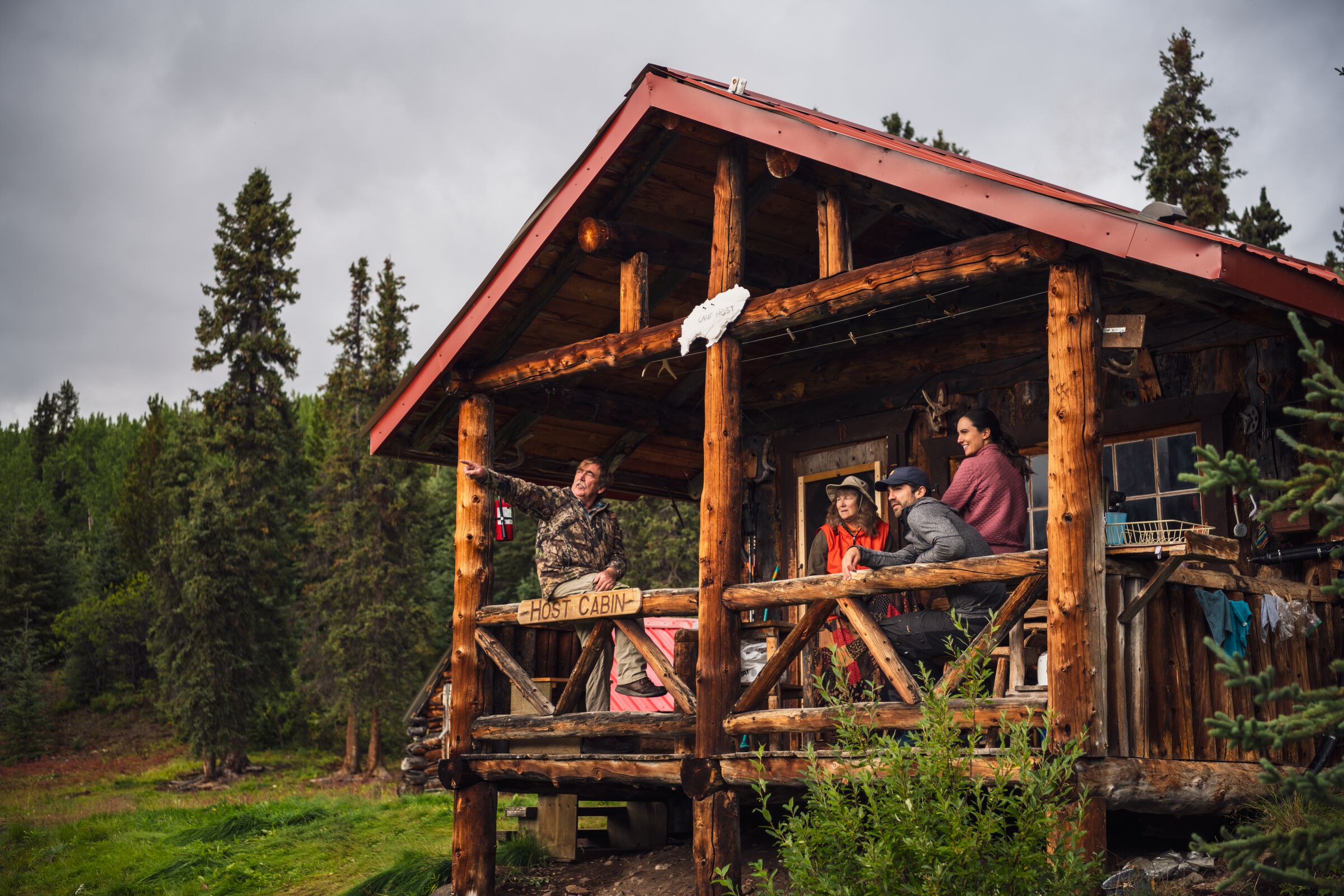 People gathering on the porch of a rustic host cabin looking out at the vast wilderness that surrounds Cold Fish Lake Camp in Spatsizi Plateau Wilderness Provincial Park.