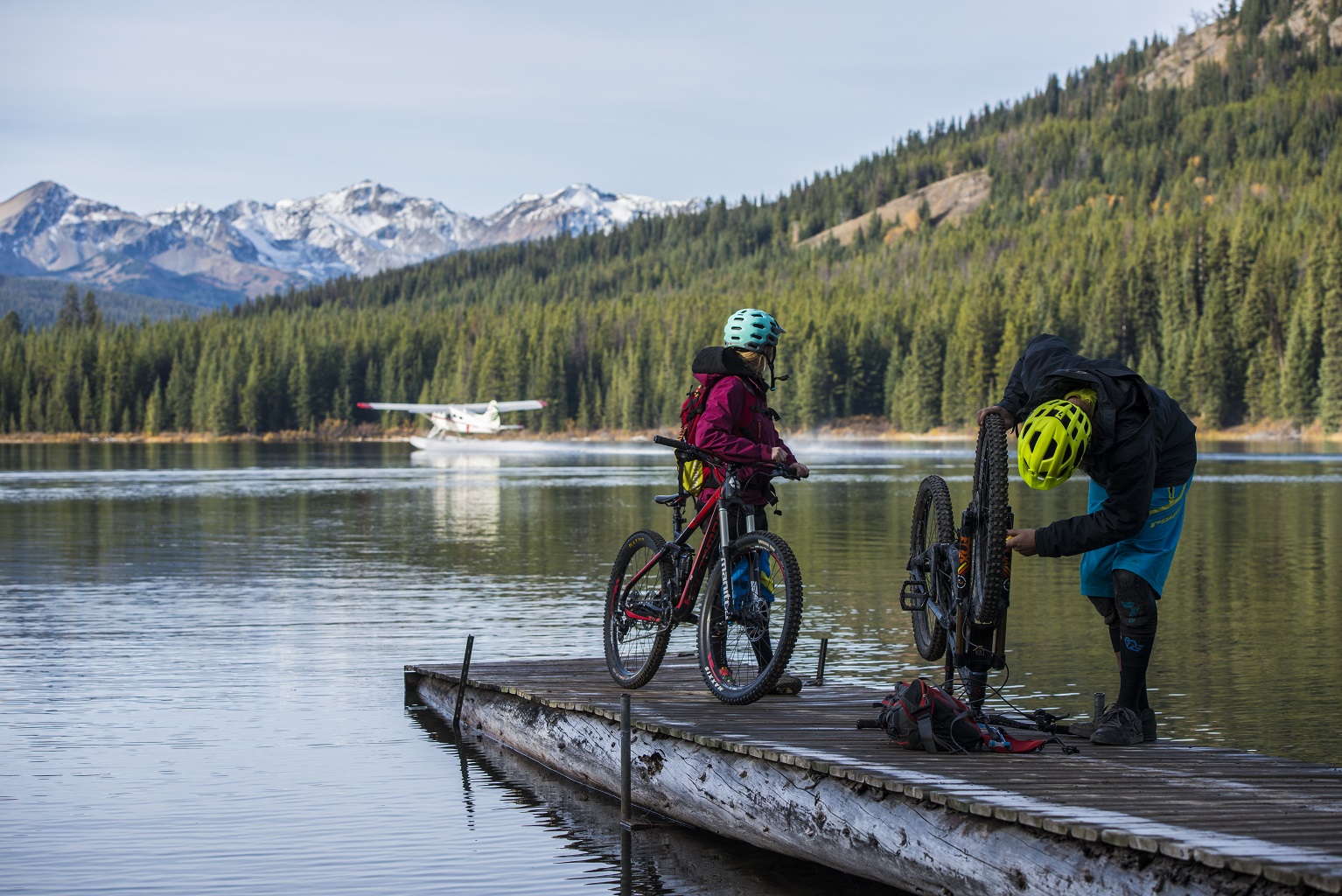 Two people with mountain bikes on a dock having been dropped off by a floatplane.