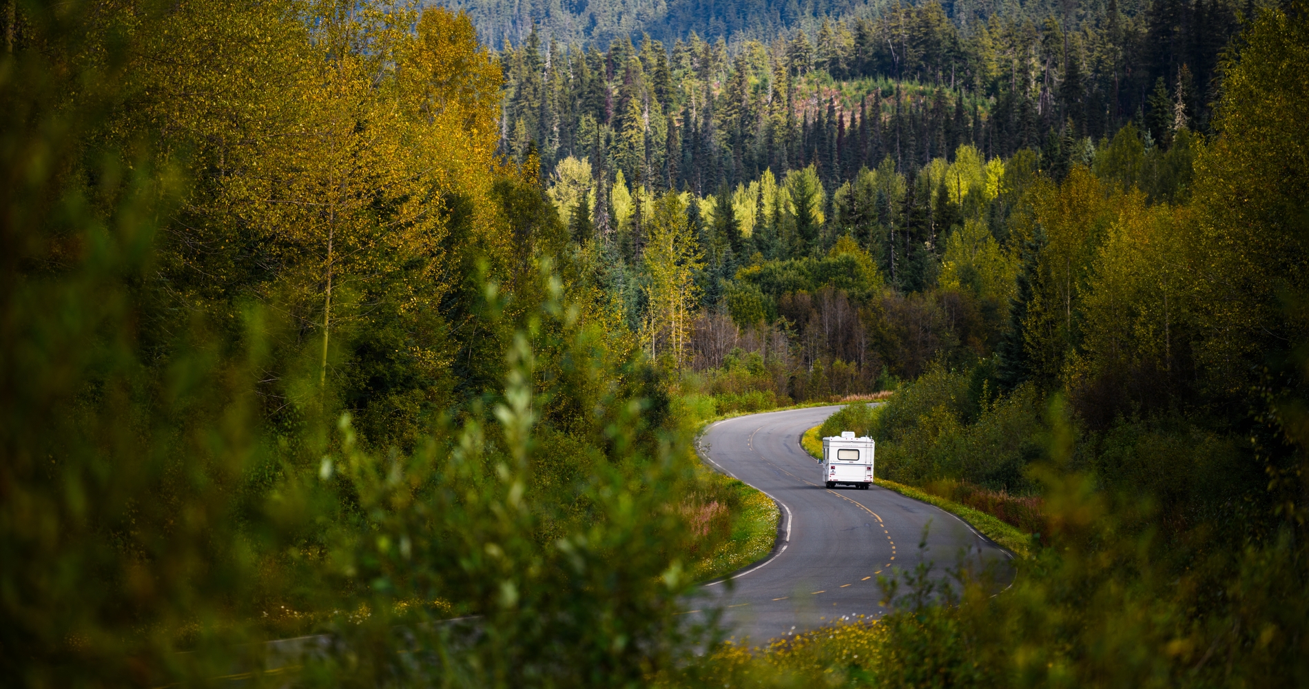 An RV drives down a winding highway surrounded by great wilderness.