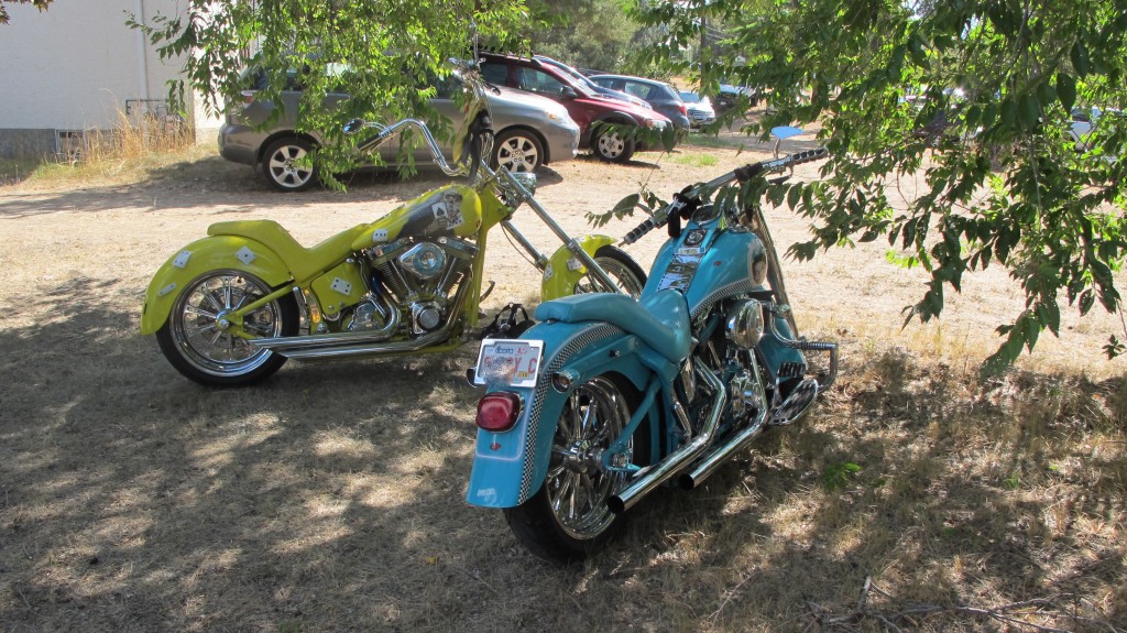 A bright yellow and bright blue motorcycle parked next to each other under a tree.