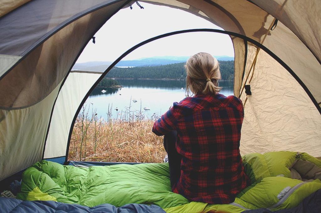 A woman in a plaid shirt sits in her tent, looking out over the water.