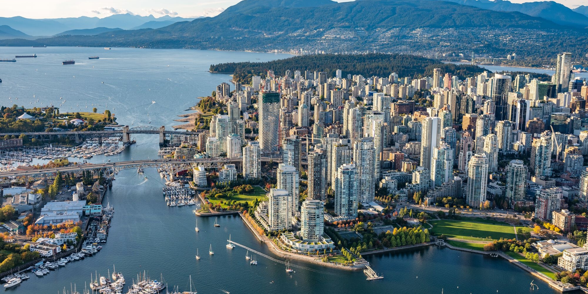 Aerial photo of downtown Vancouver at sunset. The ocean surrounds the landscape, boats fill the marinas and harbour. Both Burrard Bridge and Granville Bridge are seen on the left.