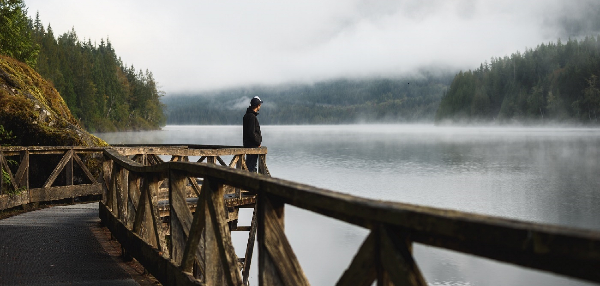 A person stares out at Inland Lake from a bridge lookout on a misty day