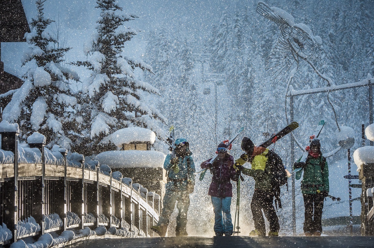 A group of skiers walks through Whistler Village with gear over their shoulders as the snow falls heavily.