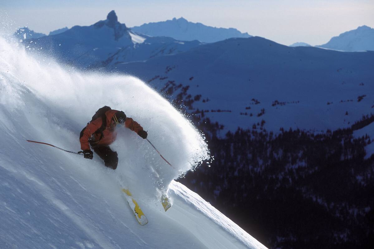 A skier does a powder slash at Whistler Blackcomb with the Back Tusk landmark in the background.