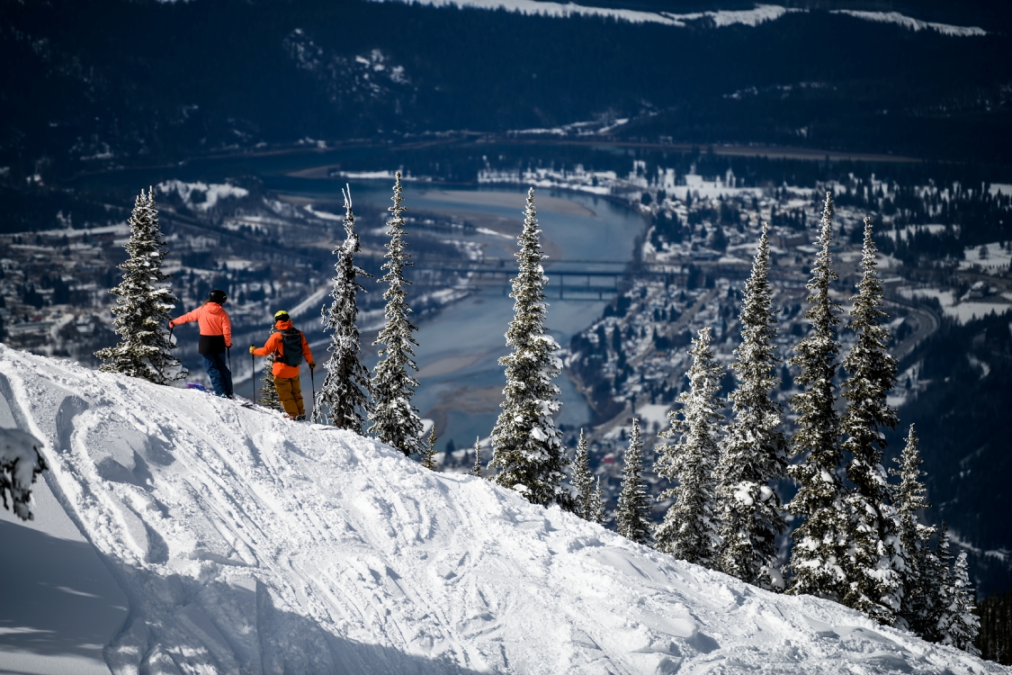 A pair of skiers look down to the town of Revelstoke and Columbia River.