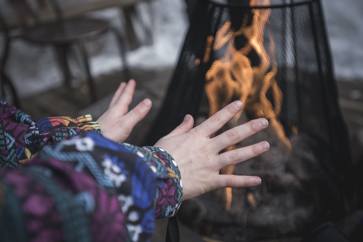 A person warms their hands by an outdoor electric fire. They are wearing a colourful patterned sweater.