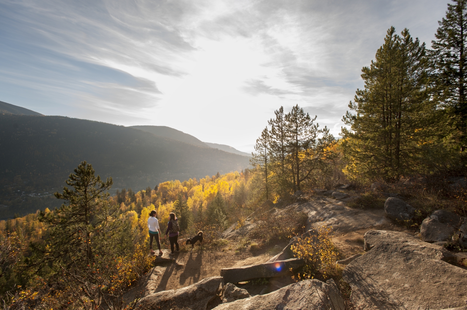 Two hikers and a dog walk along the Pulpit Rock Trail in the fall.