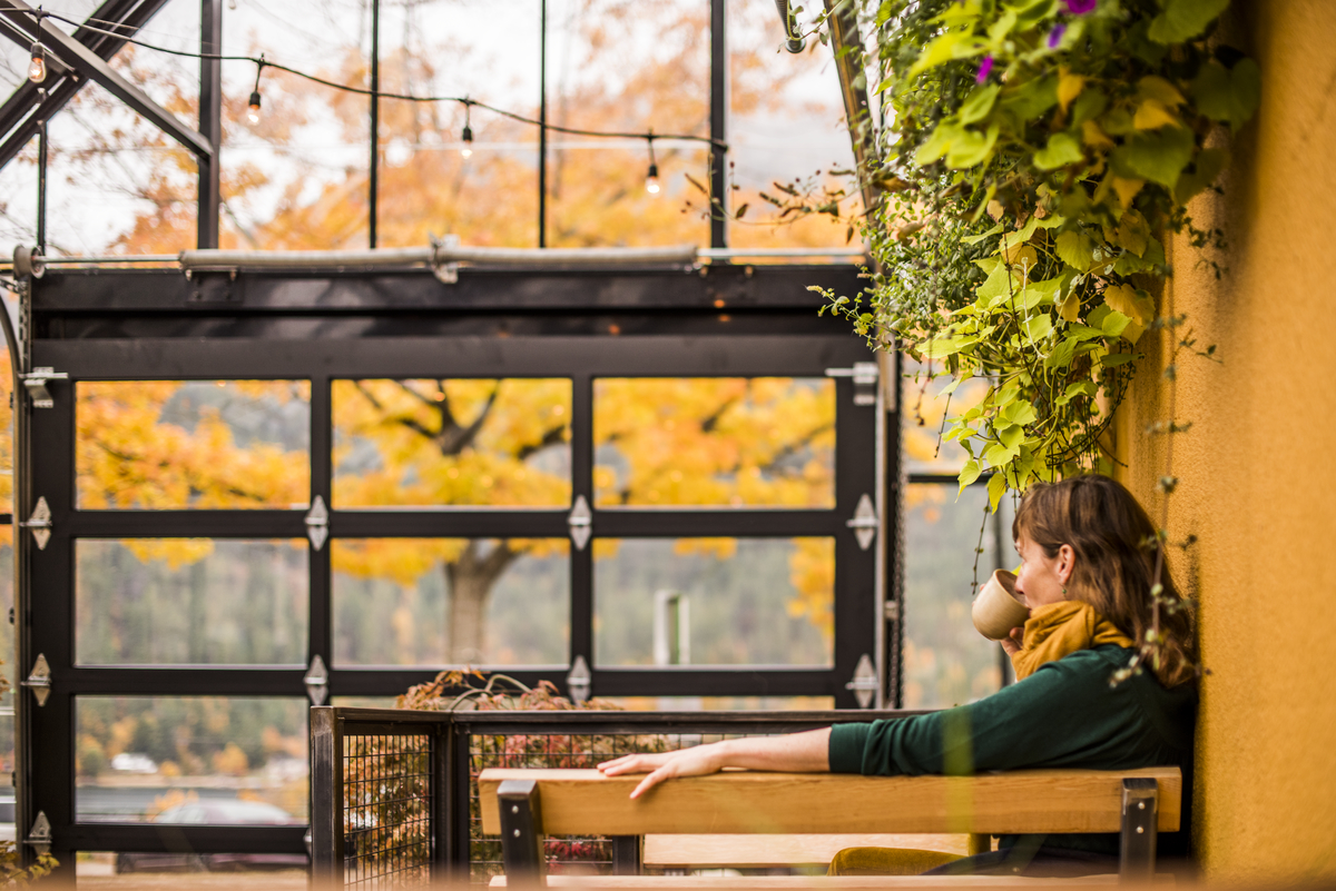 A women sips a coffee and looks out a window at the fall leaves at Empire Coffee in Nelson