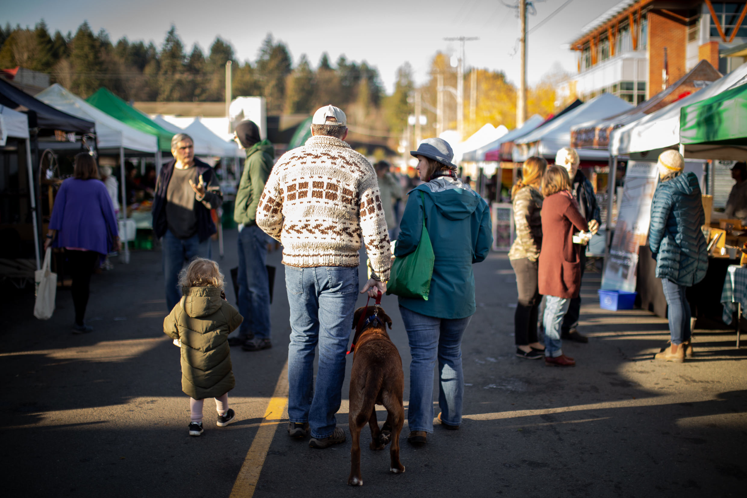 A group of people walk with their backs to the camera walk through the Duncan Farmers Market