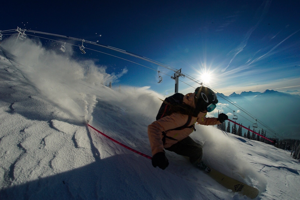 A close up of a skier on a deep turn with the chair lift behind them