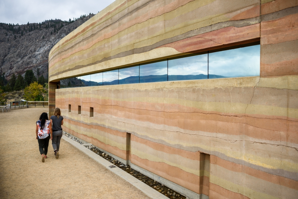 Two people walk past the outside of the Nk'Mip Desert Cultural Centre. 