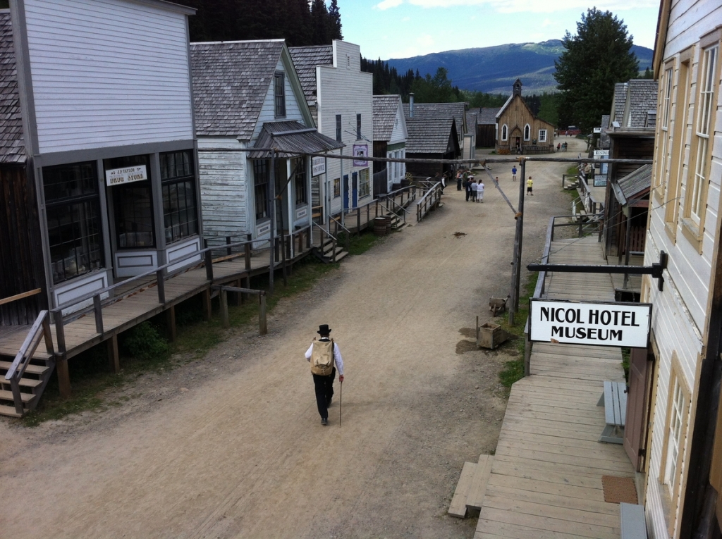 A person walks down the street of Barkerville Historic Town. There are children and other people at the end of the street in the distance. 
