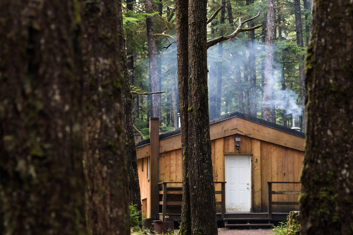 Smoke comes out of a chimney of the Hiellen Longhouse Village. The wood cabin is surrounded by trees in in Naikoon Provincial Park