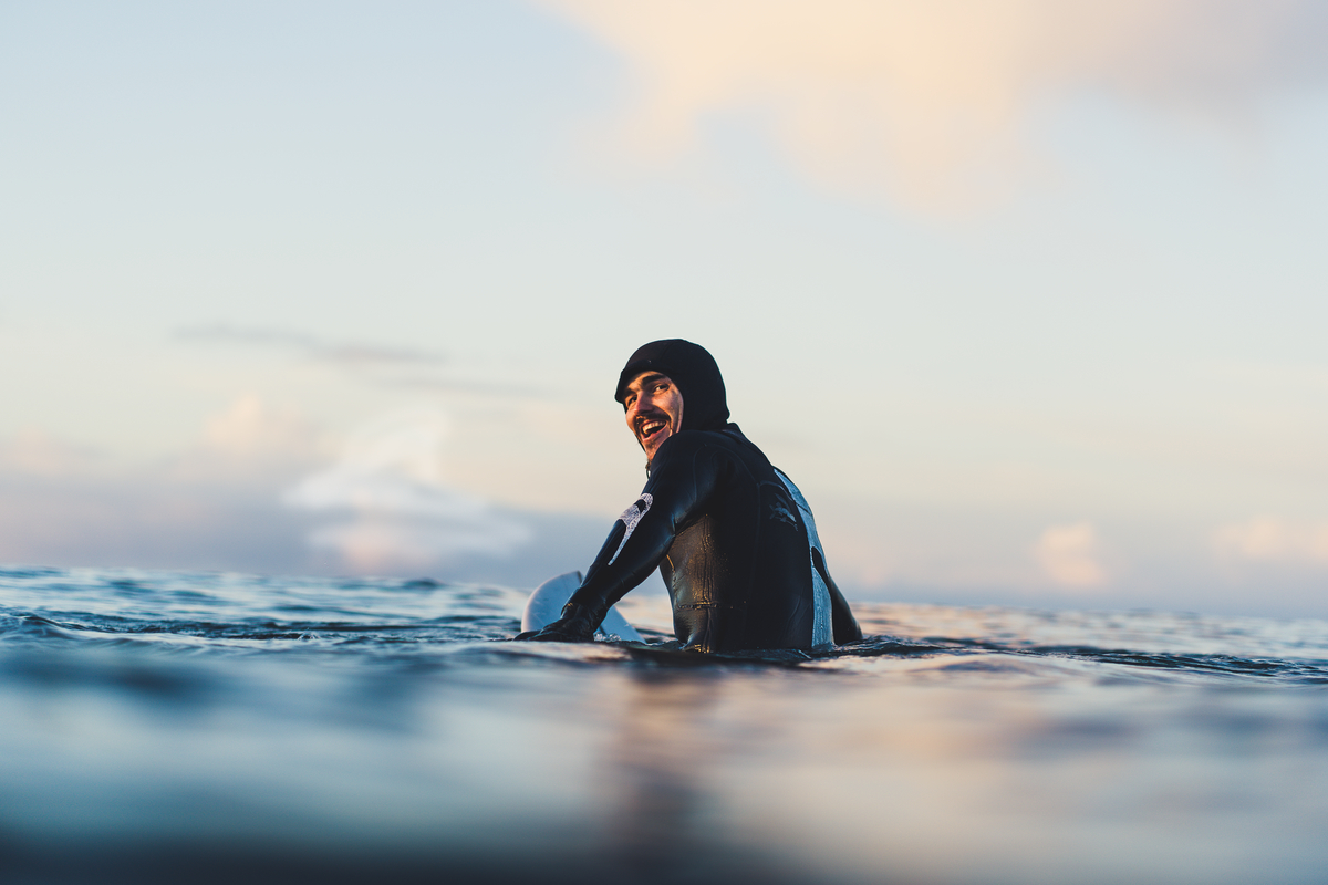 A surfer in a black wetsuit looks back at the camera from the water.