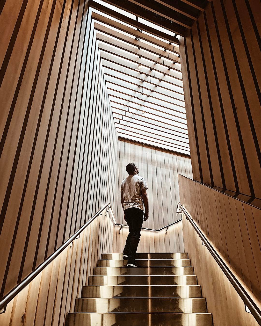 A man looks up at the wood slat ceiling from the top of a staircase inside the Audain Art Museum