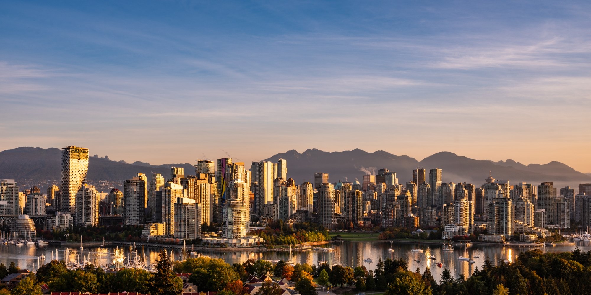 Aerial photo of Vancouver's skyline at sunset. The light reflects off the buildings and the sky glows behind the mountains in the distance.