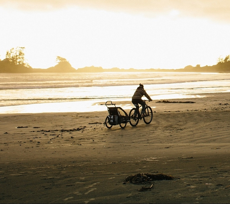 A person on a bike pulls a trailer long the beach.