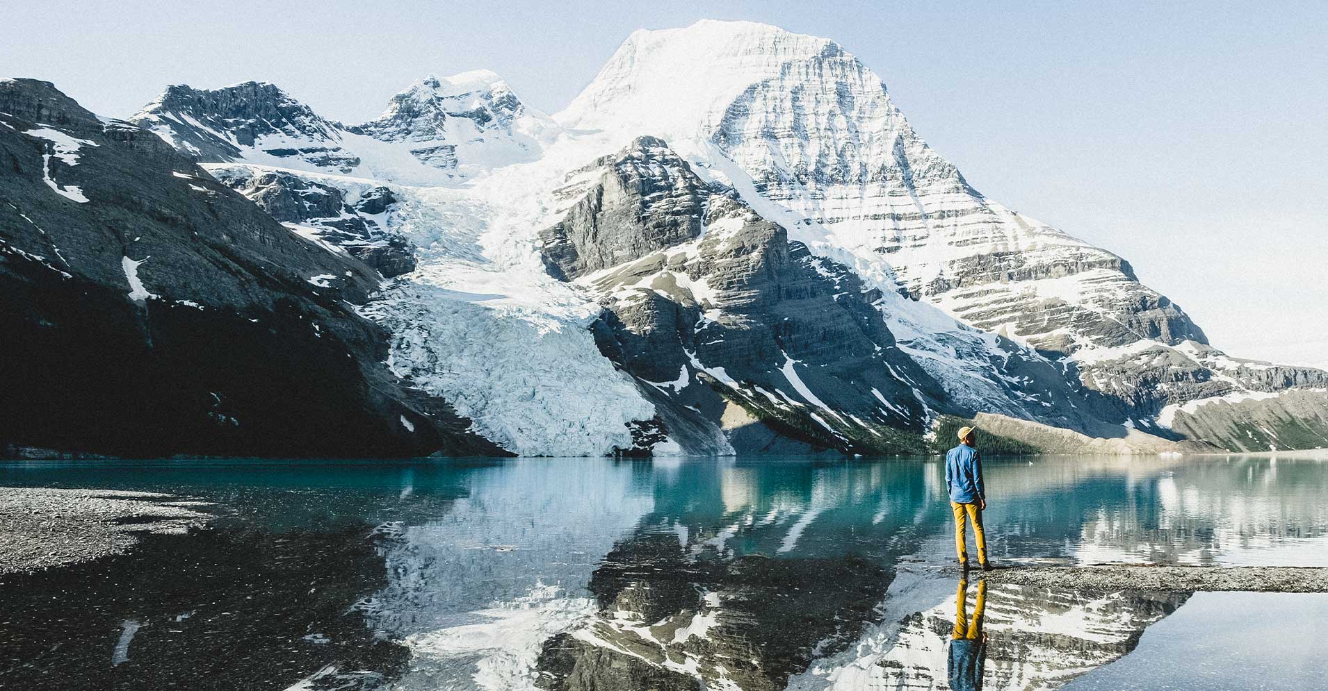 A person stands by a lake looking out at Mount Robson