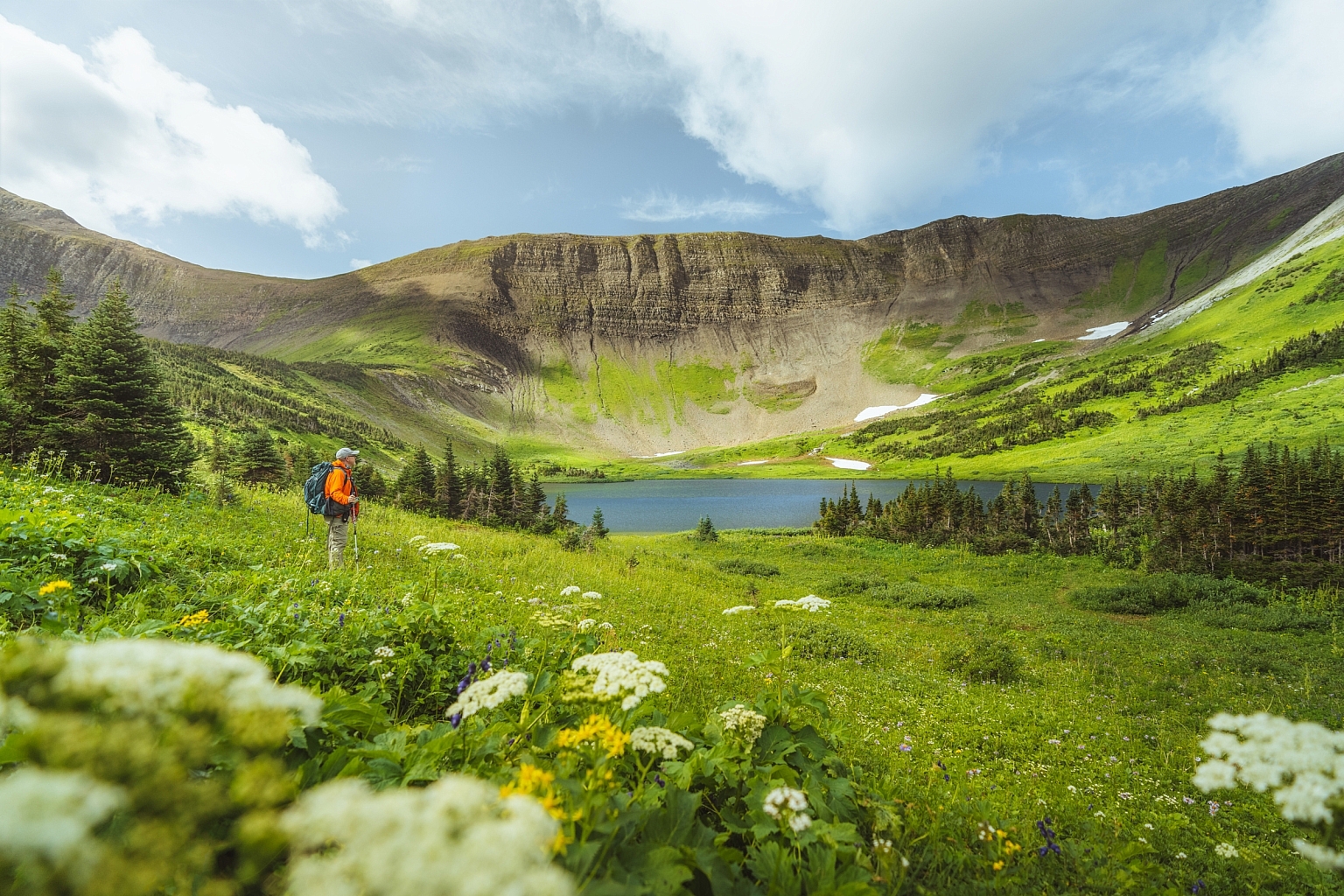 A hiker in the foreground walks past a lake with a mountain ridge behind.