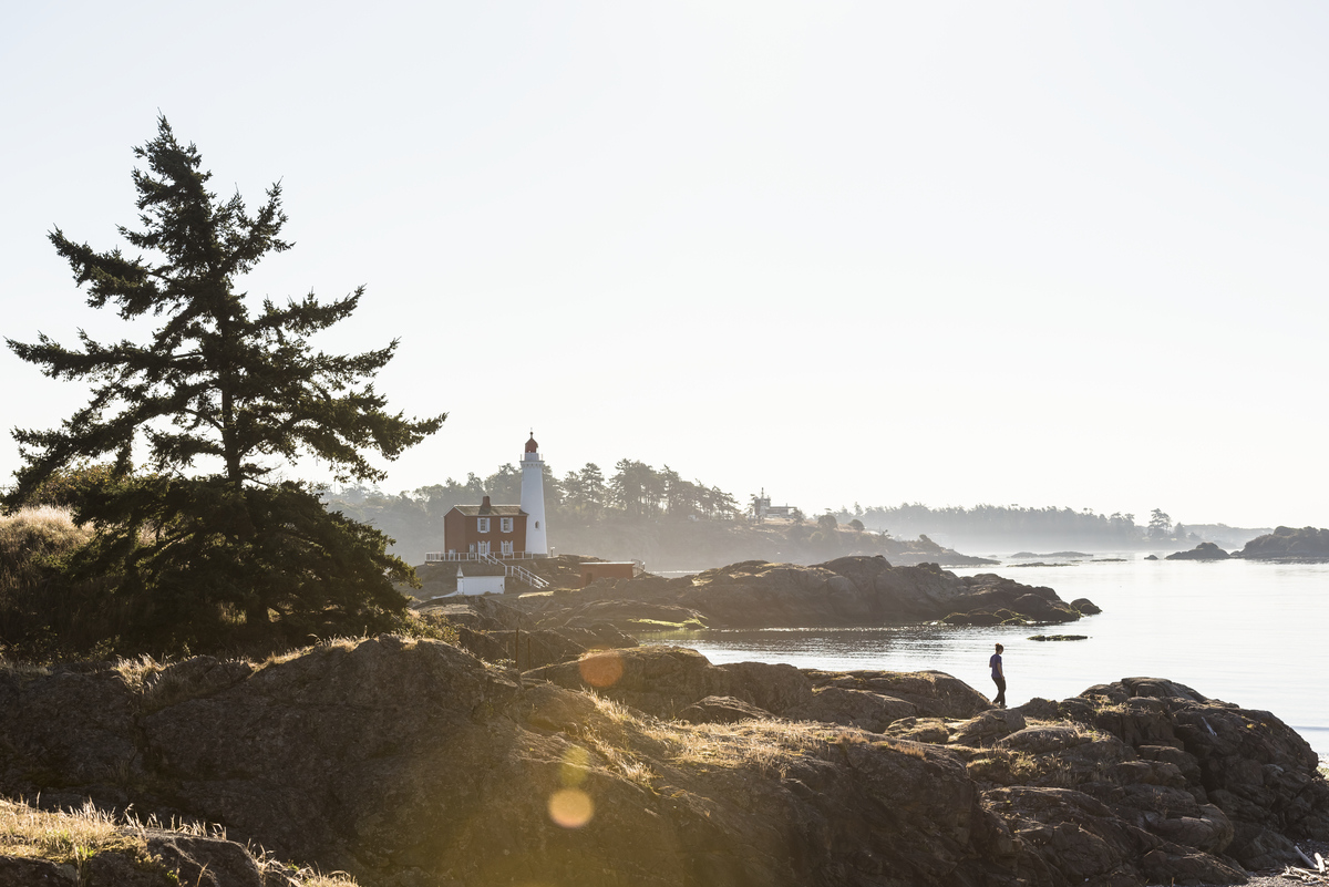 A lighthouse on the shoreline. A person looks out from the rocky outcrop.