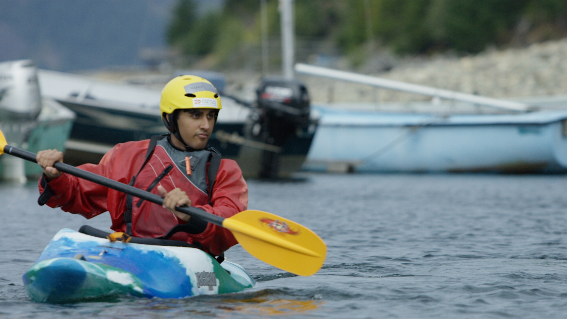 A close up of a kayaker in a red jacket and lifejacket paddles near the shoreline of the Campbell River