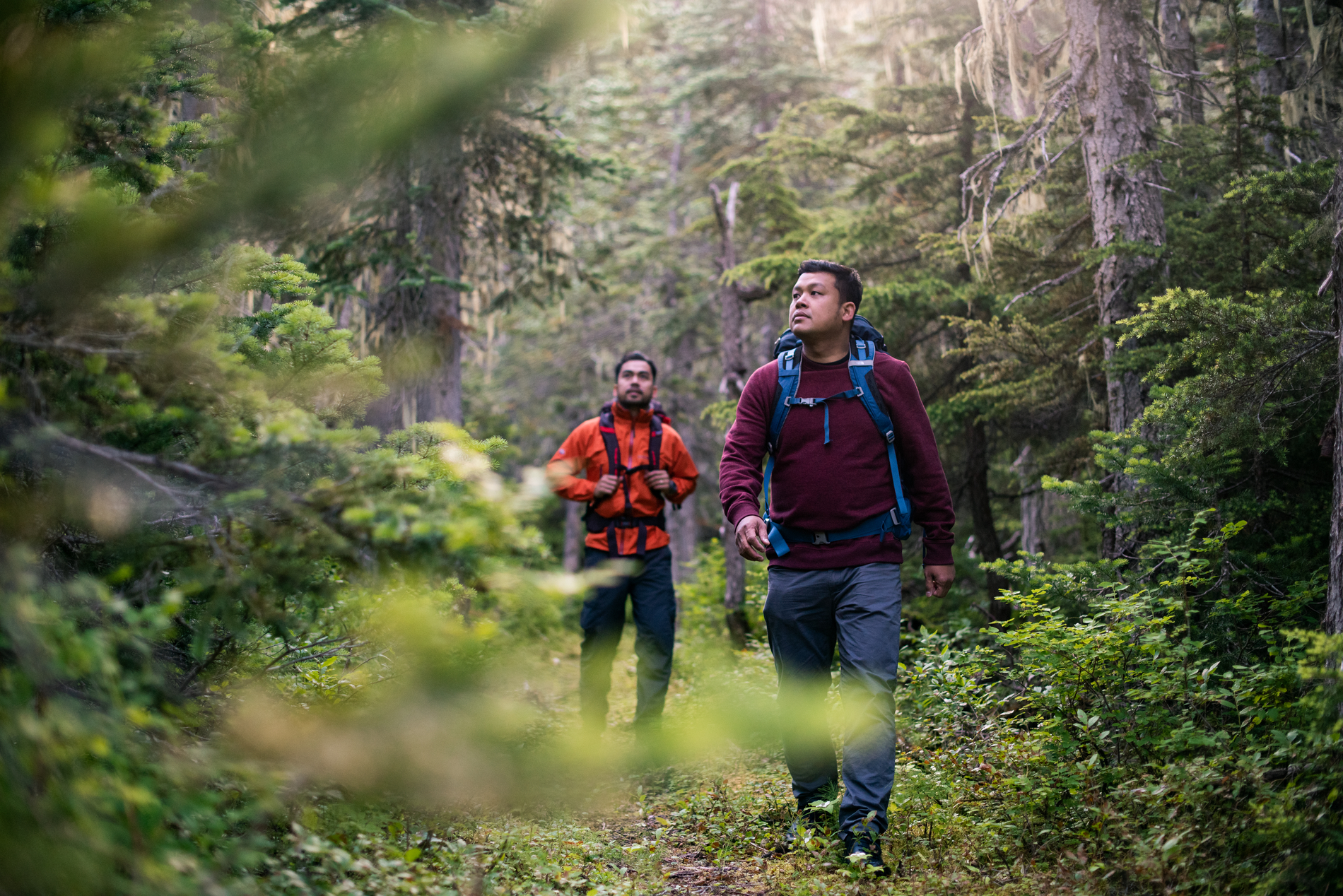 Two men hiking in Burnie-Shea Provincial Park. They are each wearing a backpack and different shades of red, long sleeve tops.