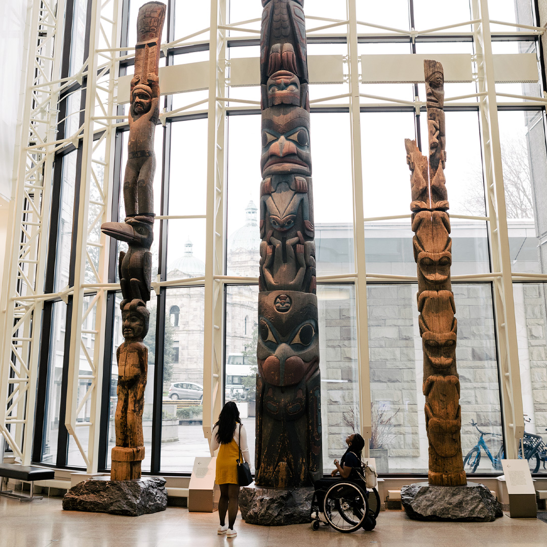 Two people gaze up at a collection of totem poles inside the Royal BC Museum
