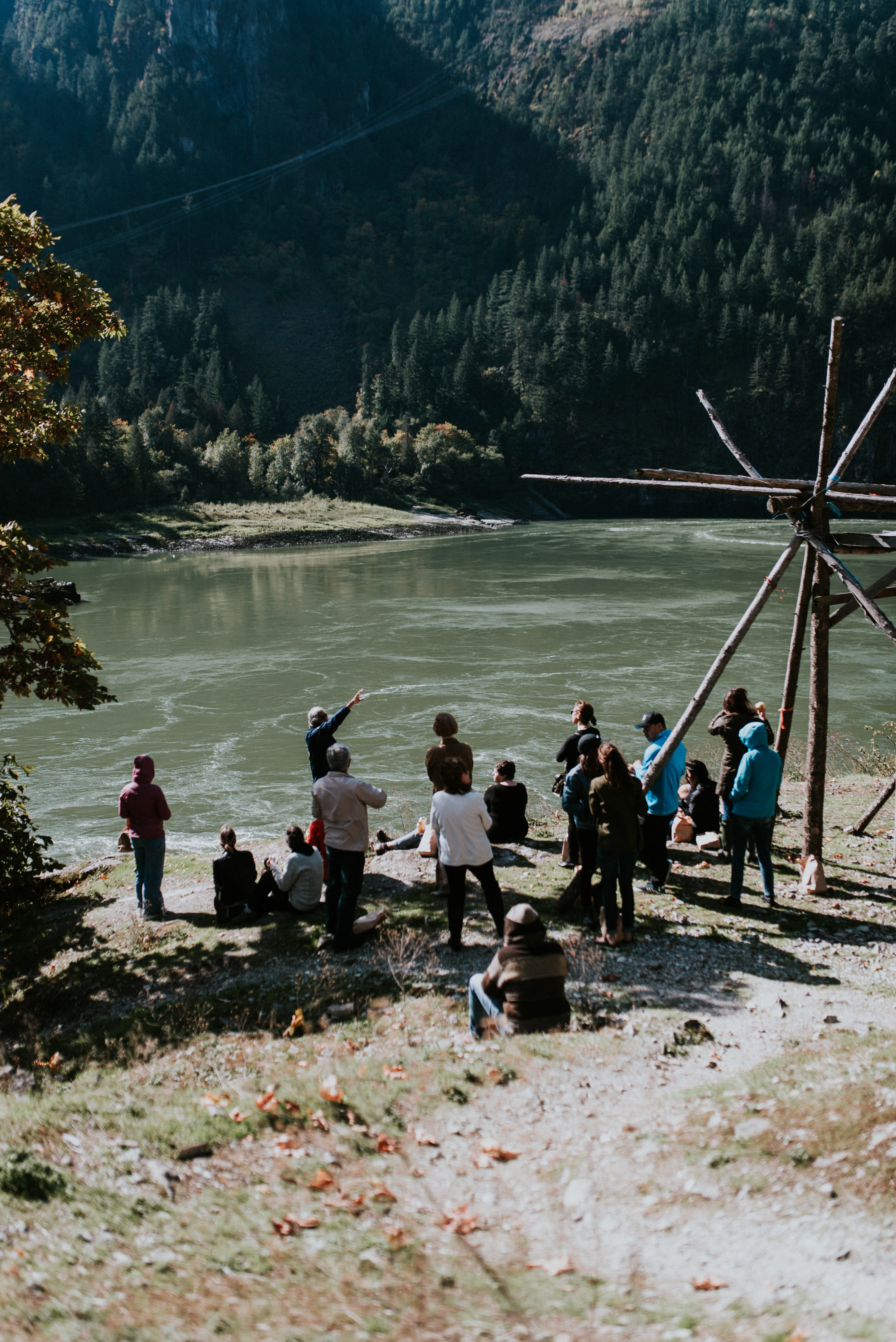 A group of tourists people stand along the river to learn more about the traditions of the Stó:lō people.