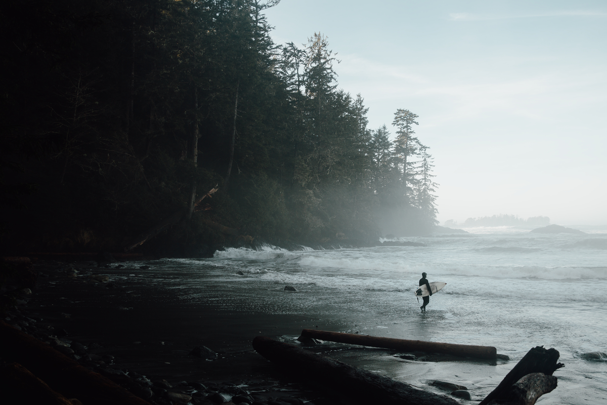 A person walks into the ocean holding a surfboard in Florencia Bay in Ucluelet