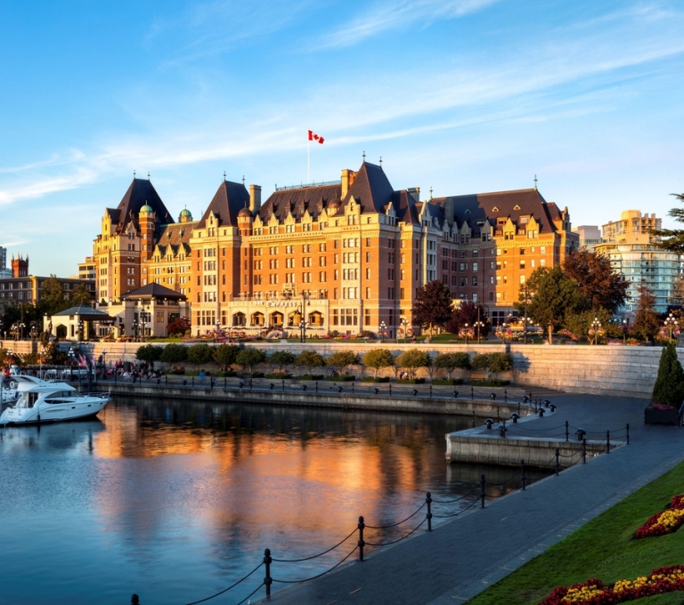 The Fairmont Empress Hotel sits lit up by sunshine. The hotel is directly in front of the harbour.