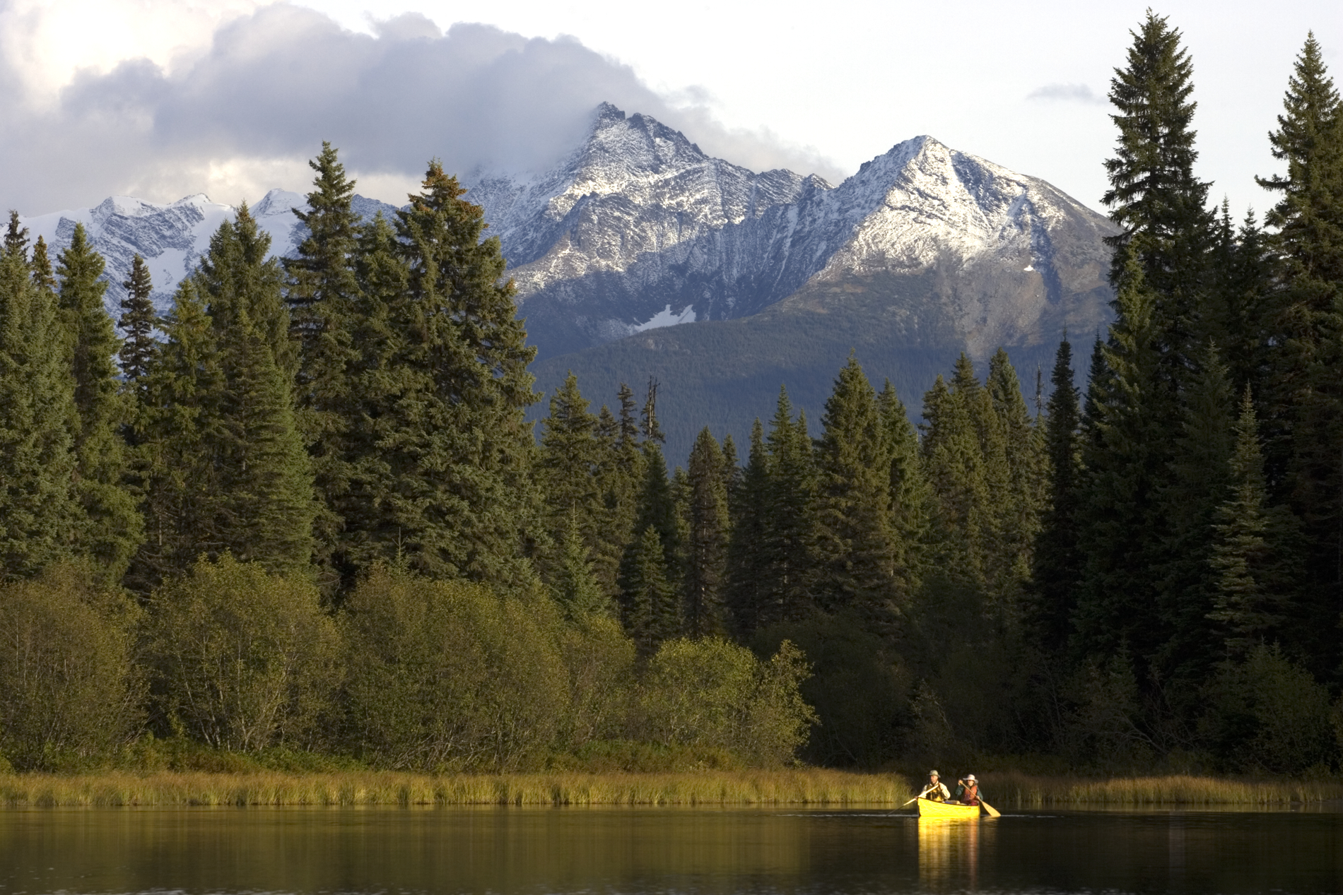 Couple canoeing with views of the mountains at Babcock Lake in Bowron Lake Provincial Park.