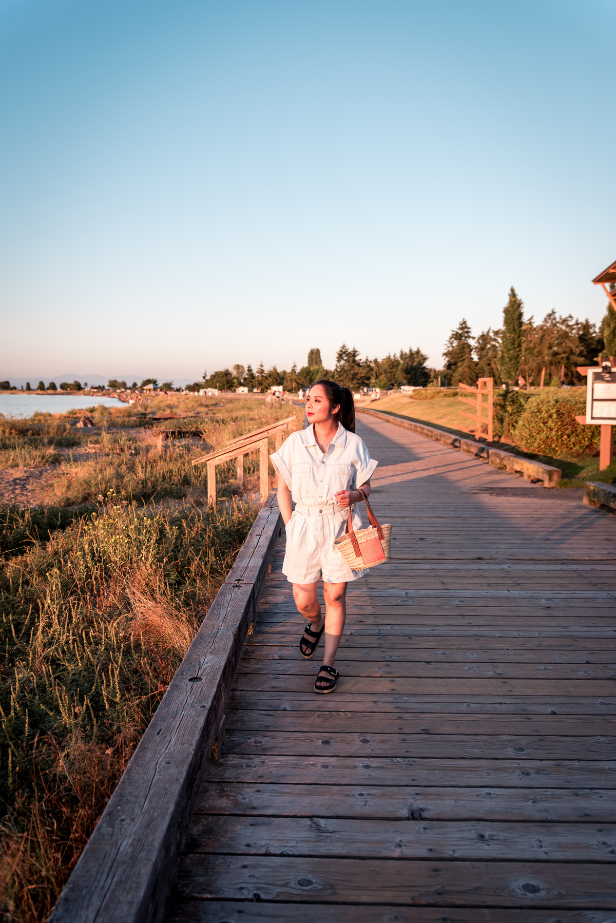 Yvonna Chow walks down a boardwalk next to the ocean. The sun is shining on her as she approaches the camera.