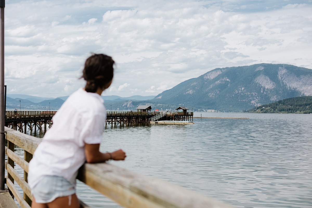Mirae looks out from the Salmon Arm Pier at the ocean and mountains in the distance. She is wearing a white t-shirt and jean shorts.
