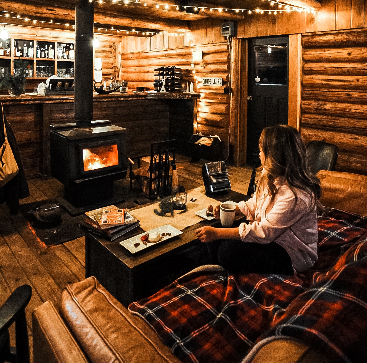 A women sits inside a wood cabin at a table sipping a drink at the Chute Lake Lodge
