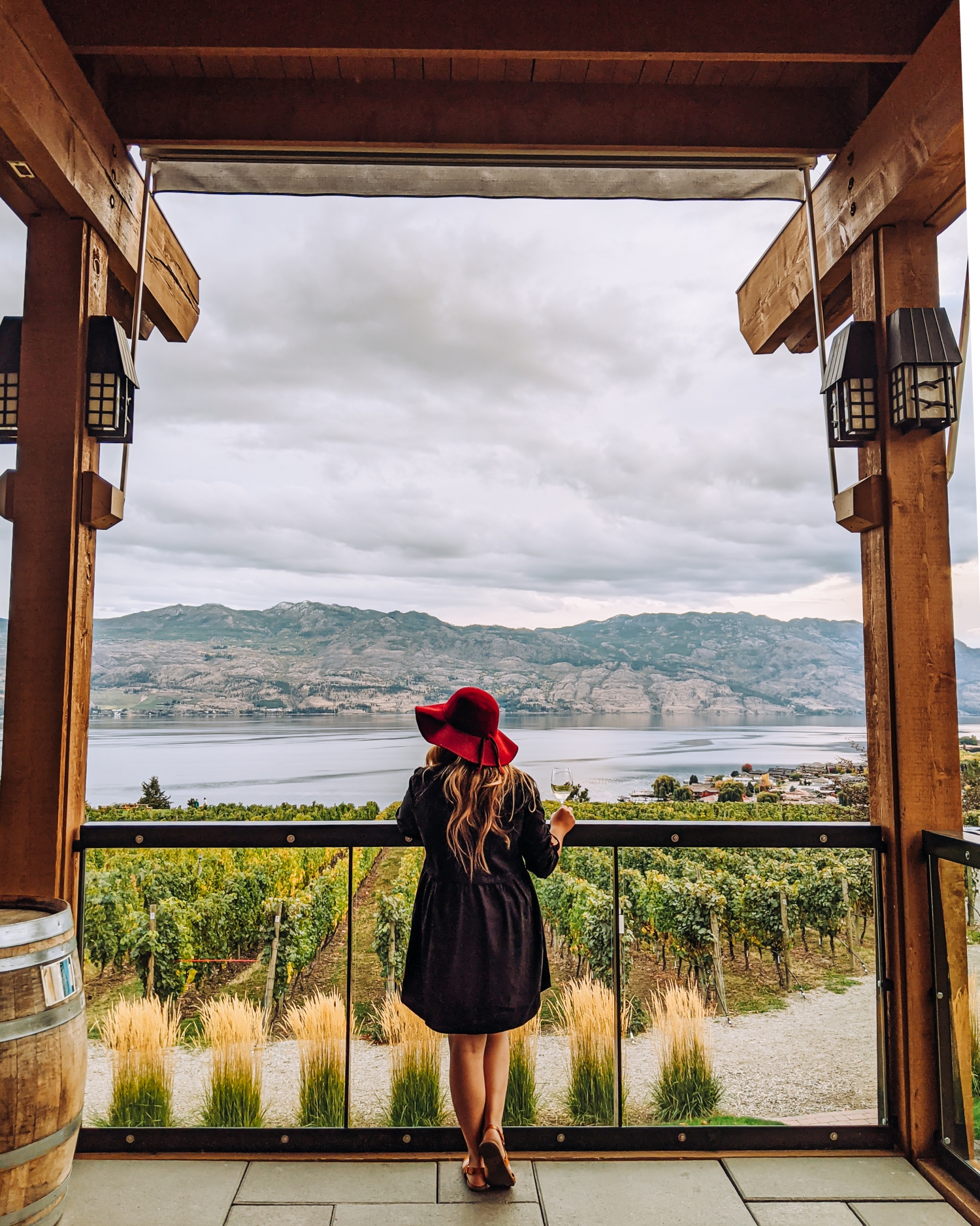 A women wears a red hat and a black dress and is looking out at the vineyards at the Quails' Gate Estate Winery in Kelowna.