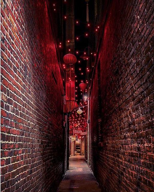 Two brick walls line a narrow walkway with red lights hanging above in Victoria's Fan Tan Alley