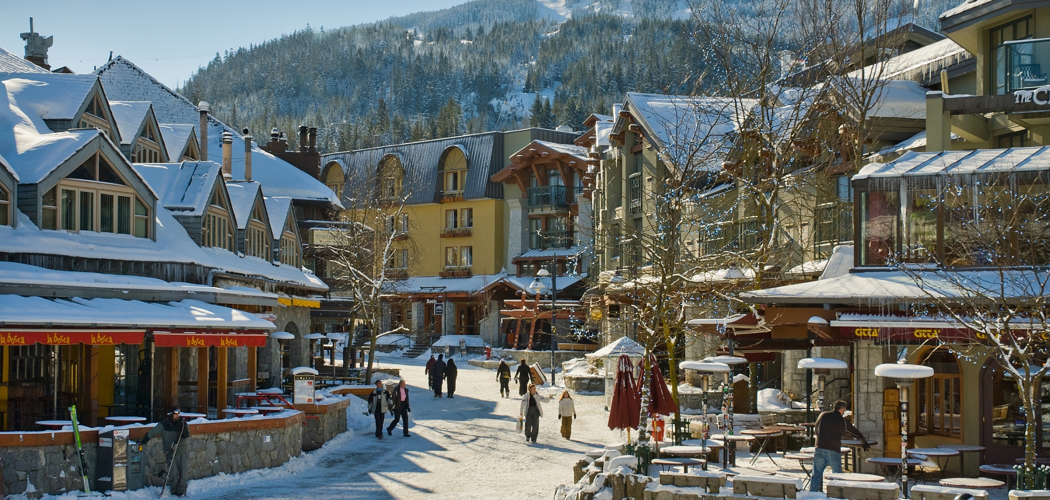 People walking through Whistler village in winter. Snow covered buildings.