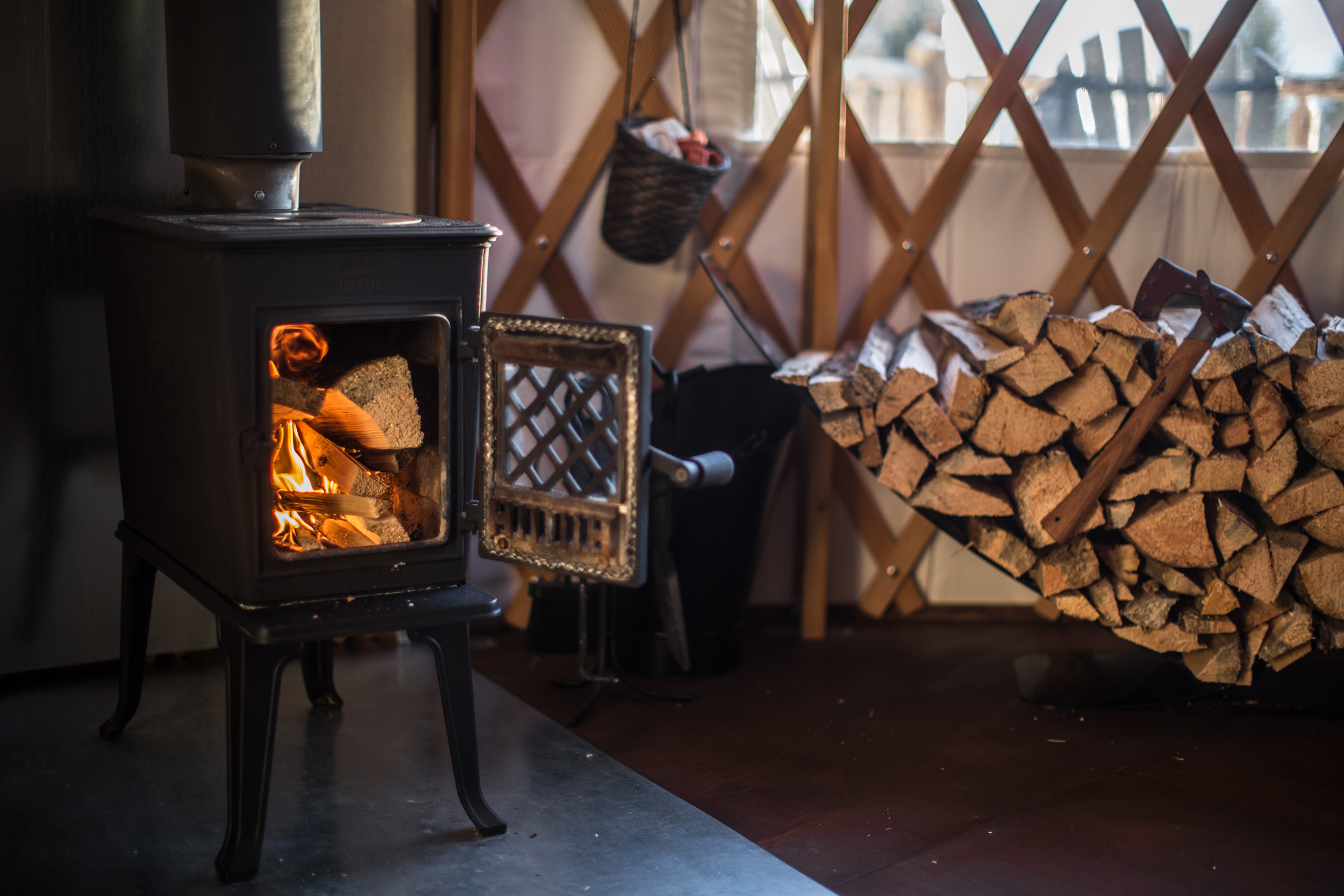 A wood burning fire and a stack of firewood against the wall inside a yurt