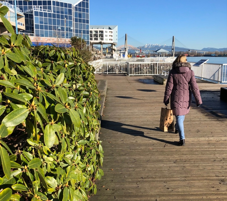 A person walks down a boardwalk towards a glass building in New Westminster.