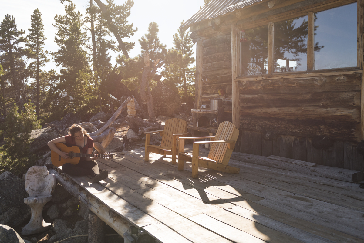 A guitarist sits in front of a cabin at Nuk Tessli Wilderness Experience on a sunny day.