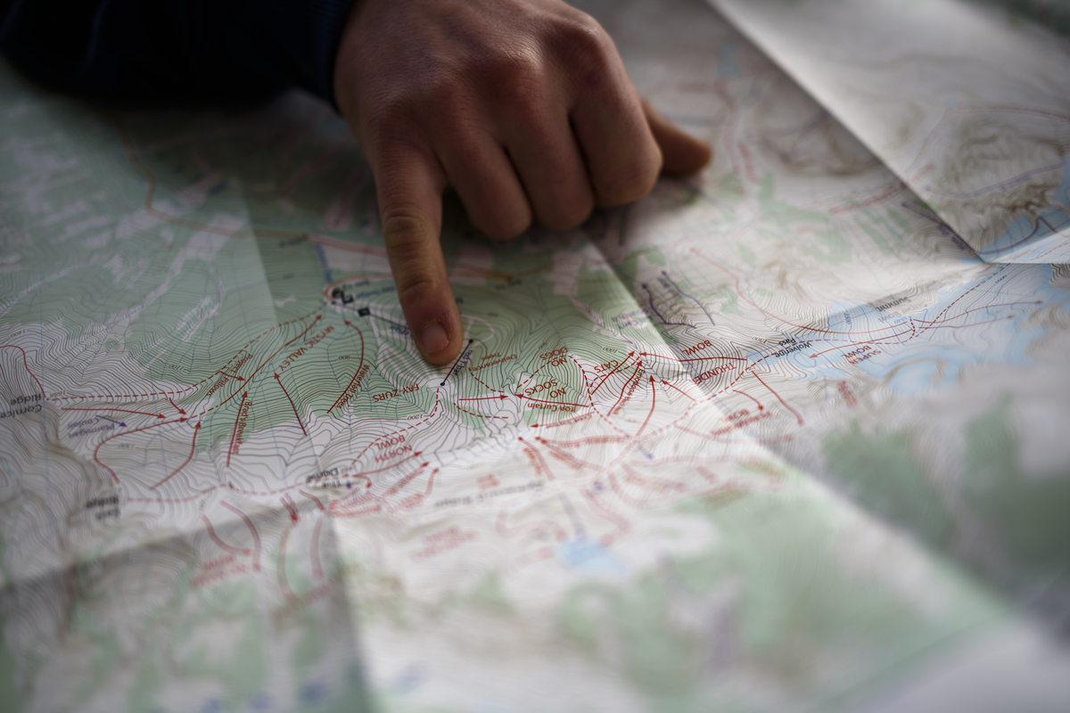 A person's pinky finger points to a specific spot on a paper map.