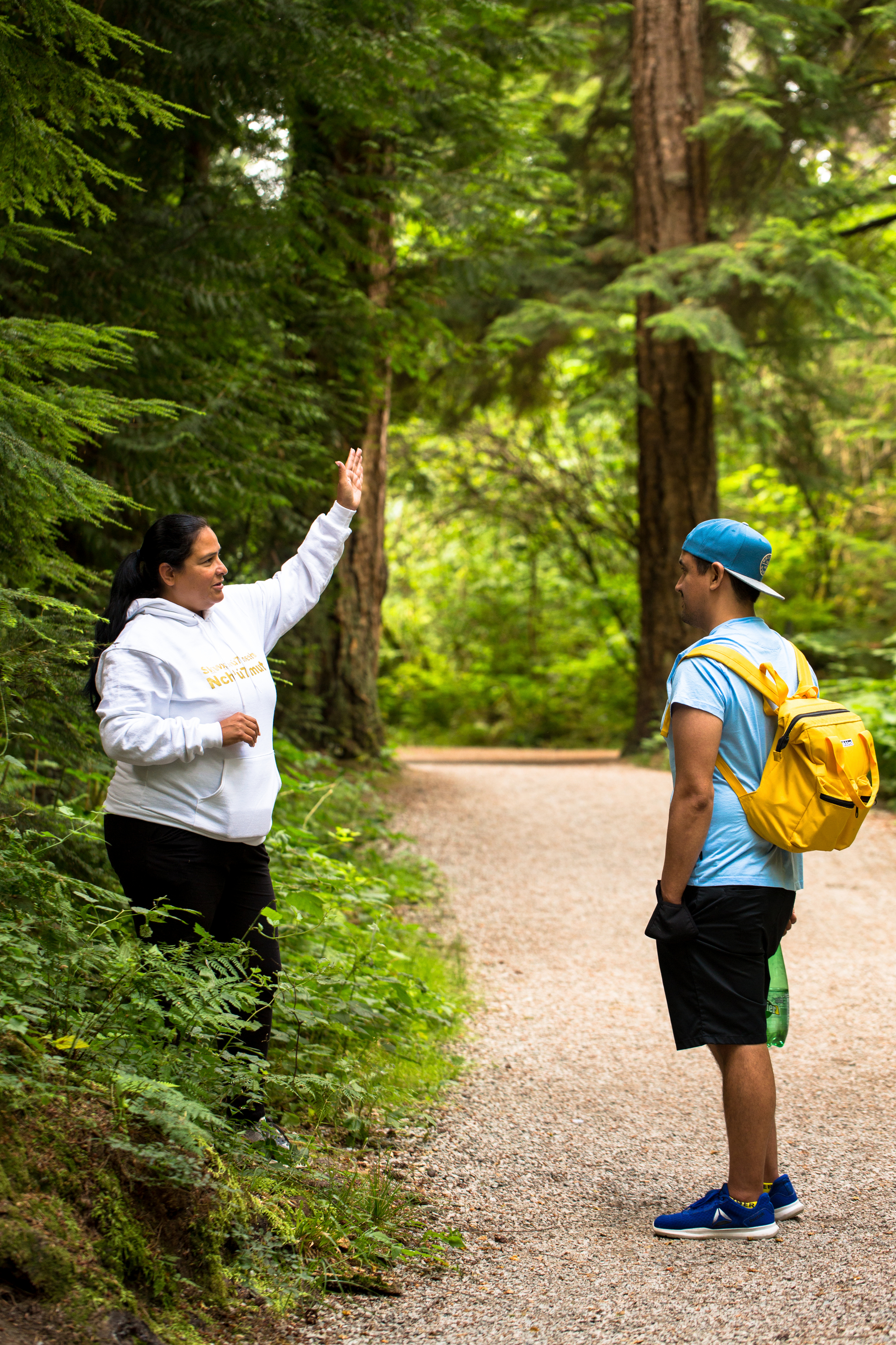An Indigenous interpreter points to the trees to a tourist. They are standing on a path in Stanley Park.