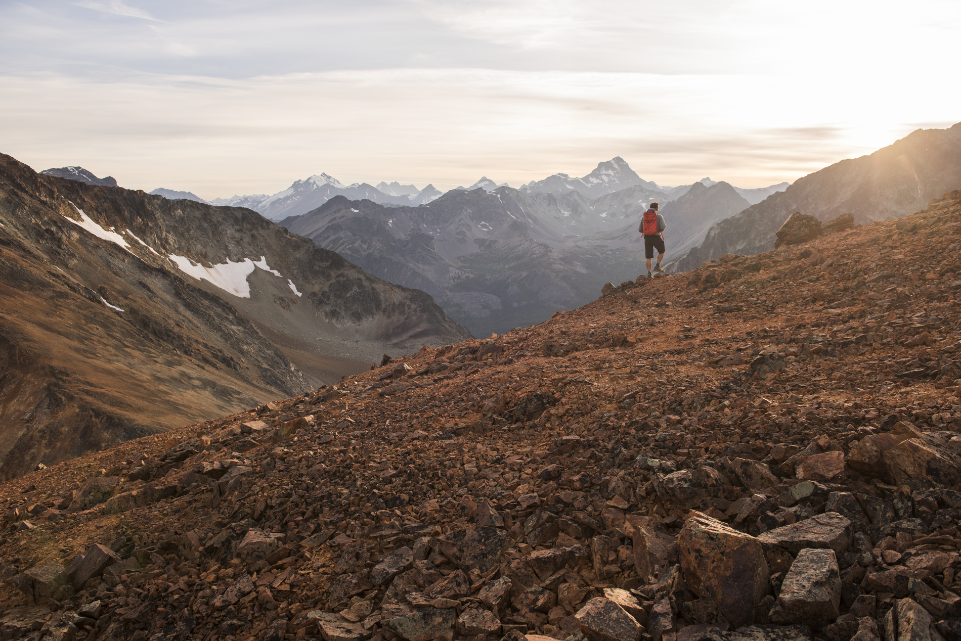 A hiker in the distance amid a rocky mountain landscape. The sun is setting in the range.