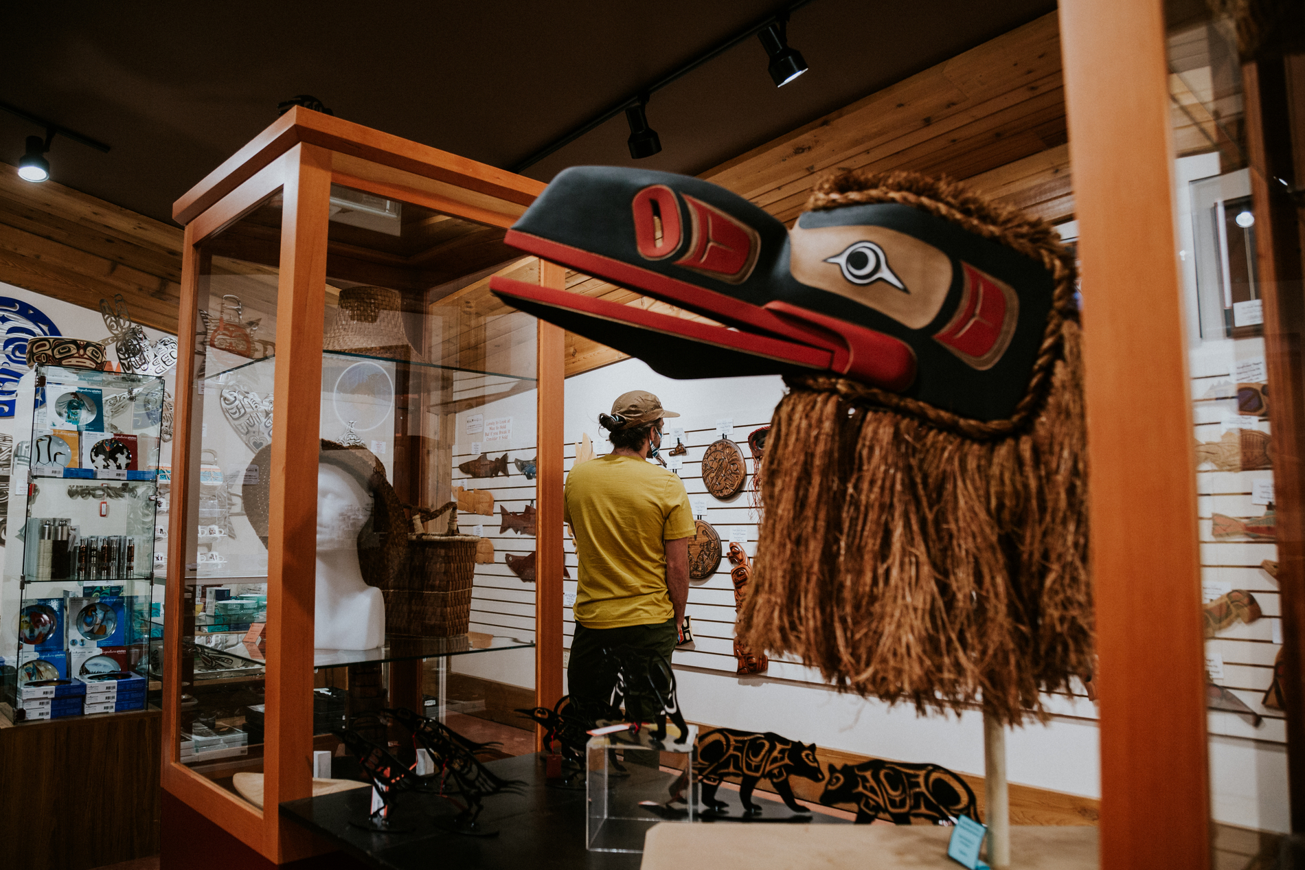 A collection of Indigenous art in glass cases and on the walls. A man examines a piece on the wall in the background.