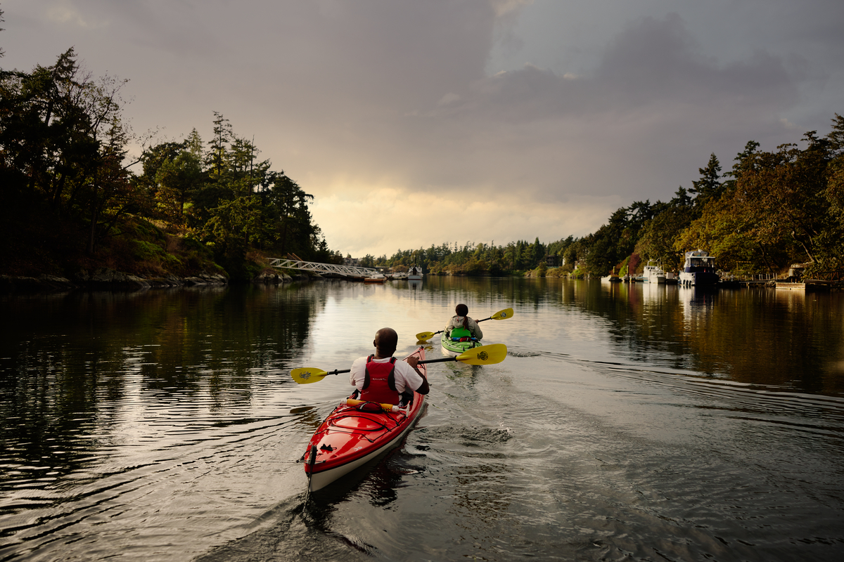 Two people are kayaking down a river at sunset