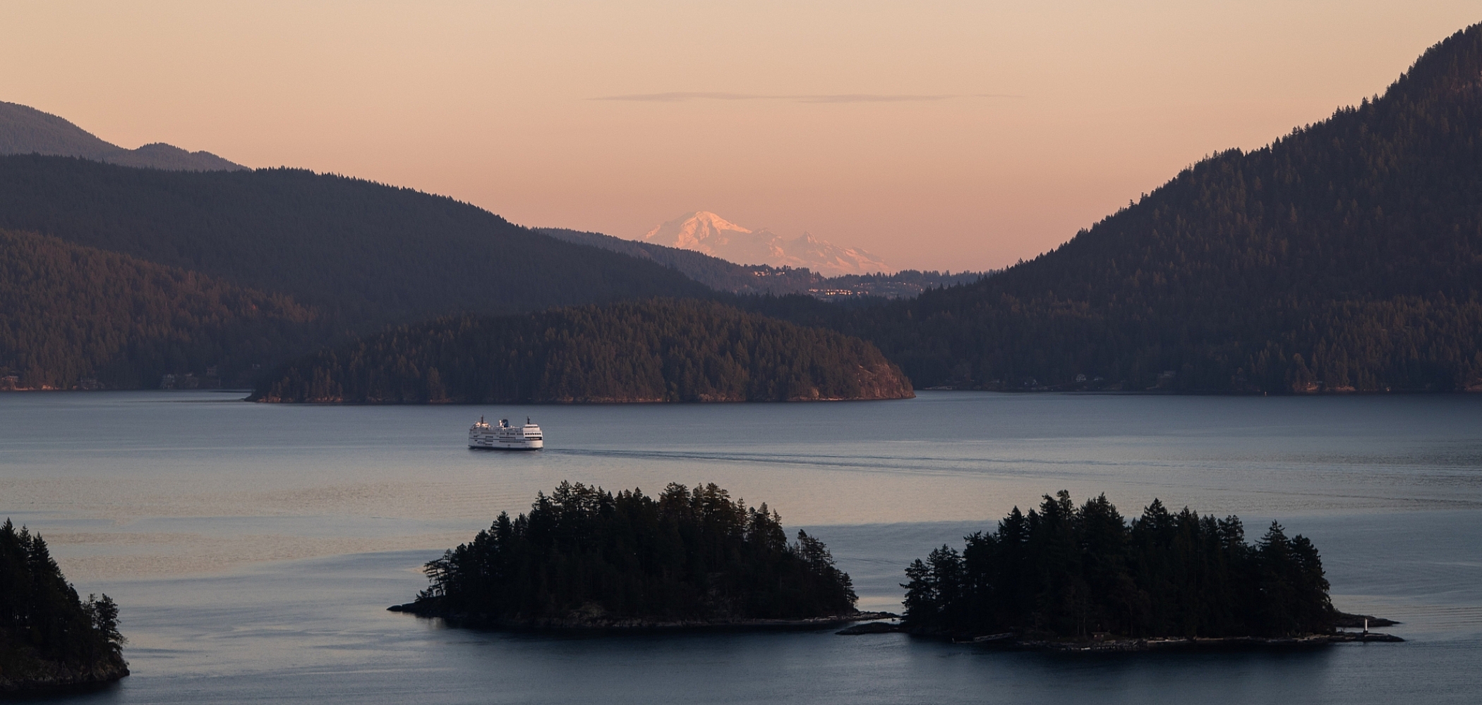 Aerial view of a BC Ferry sailing past two small islands at sunset