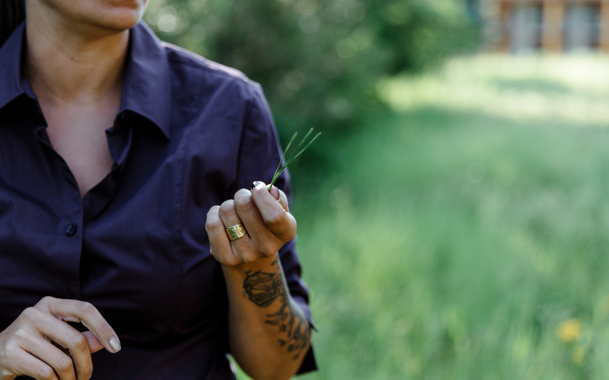 A person is seen holding a piece of grass in their hand (their head is not shown in the frame).